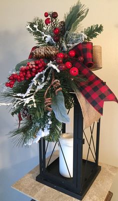 a christmas lantern decorated with holly, berries and pine cones is sitting on a table