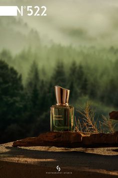 a bottle of perfume sitting on top of a wooden table next to a forest filled with trees