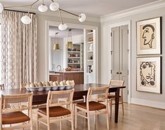 a dining room table and chairs with artwork on the wall behind them in front of a window