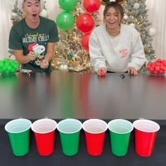 two people sitting at a table with red and green plastic cups in front of them