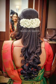 the back of a woman's head with flowers in her hair and an orange saree