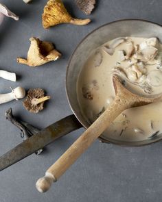 a wooden spoon in a bowl filled with mushroom soup next to mushrooms and cloves