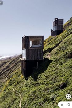 two wooden buildings sitting on top of a lush green hillside