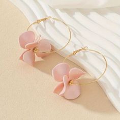 two pink flowers are hanging from gold hoop earrings on top of a white bed sheet