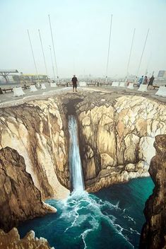 people are standing on the edge of a cliff with a waterfall in front of them