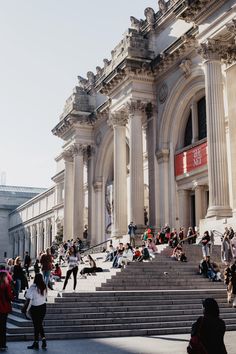 many people are sitting on the steps in front of a building with columns and arches