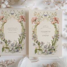 two wedding cards with flowers and butterflies on them, sitting next to some dried flowers