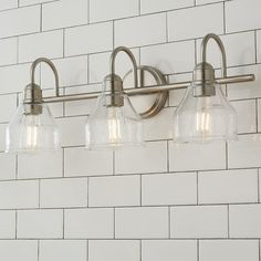 three light bathroom fixture with clear glass shades on white brick wallpapered walls and flooring