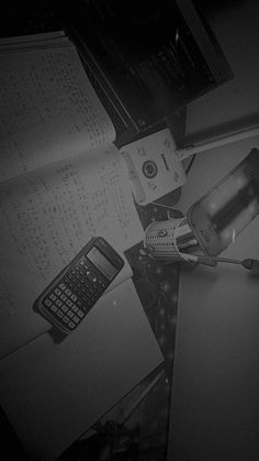 there is a cell phone, calculator and other items on the desk in this black and white photo