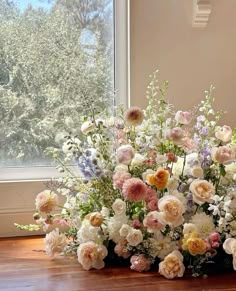 a large bouquet of flowers sitting on top of a wooden floor next to a window