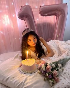 a woman laying in bed next to a cake with a candle on top of it