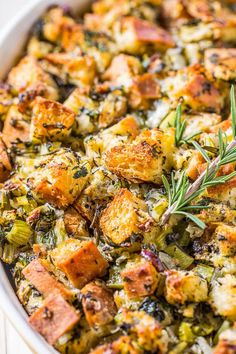 a casserole dish filled with stuffing and topped with a sprig of rosemary