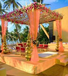 an outdoor wedding setup with pink and white flowers on the altar, gold vases and red chairs