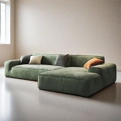 a green couch sitting in front of a window next to a white wall with two pillows on it