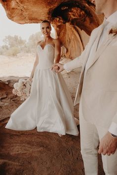 a bride and groom standing in front of a rock formation at their desert wedding ceremony