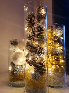 three glass vases filled with pine cones and christmas ornaments on a counter top next to each other