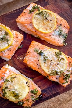 four pieces of salmon with lemons and herbs on them sitting on a cutting board