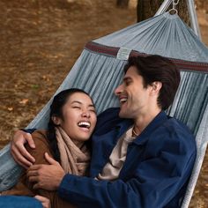 a man and woman sitting in a hammock laughing