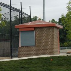 a baseball field with a small building on the side and trees in the back ground