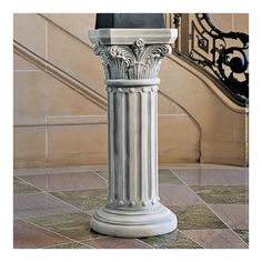 a white pillar on the ground in front of a stair case with a clock above it