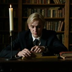 a man sitting at a table in front of a book shelf with a lit candle