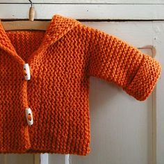 an orange knitted sweater hanging on a white door frame with a wooden hanger