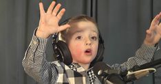 a young boy wearing headphones and holding his hands up in front of a microphone