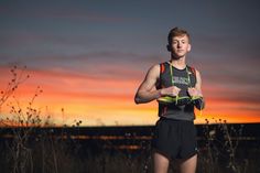 a young man standing in front of a sunset with his running gear on and looking at the camera