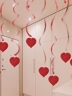 some red hearts hanging from the ceiling in a room with white cupboards and cabinets