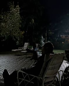 a man sitting in a lawn chair next to a pool at night