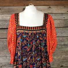 This loud and fabulous print dress is a fusion of western 1960s orange floral print and a southeast Asian sarong kebaya batik style print. The dress has a square neckline, 3/4 length puffed sleeves and a wide ruffled hem with 2 large external pockets and is 100% cotton. It is a versatile and cheerful summer piece in a roomy Size L. Blue buttons and snaps can be undone halfway down the back to step into the dress when required. There is also a wide hand stitched hem on the ruffle that allows for Multicolor Peasant Dress For Fall, Retro Orange Printed Dress, Vintage Orange Dress For Festival, Retro Summer Dresses With Paisley Print, Retro Orange Dresses With Vibrant Print, Retro Orange Dress With Vibrant Print, Vintage Multicolor Paisley Print Dresses, Vintage Paisley Print Dresses For Fall, Maxi Dress Floral