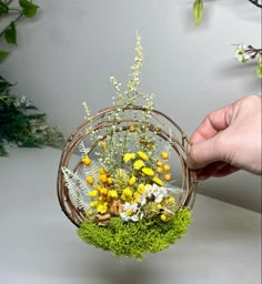 a person is holding a basket with flowers in it and moss on the inside,