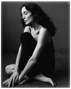 a black and white photo of a woman sitting on the floor with her hands together