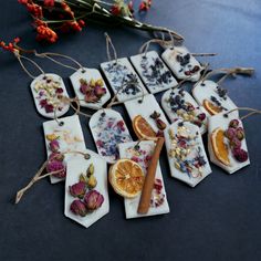 small tags with dried fruit and herbs are on a table next to orange slices, cinnamon sticks, and flowers