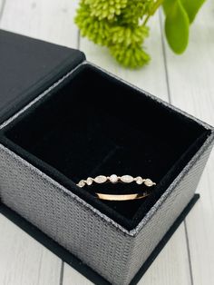 an open box with a ring inside on a white wooden table next to a green plant