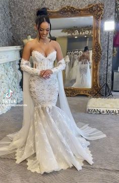 a woman standing in front of a mirror wearing a white wedding dress with long sleeves