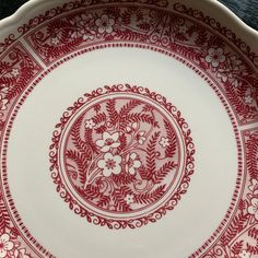 a red and white plate with floral designs on the rim is sitting on a table