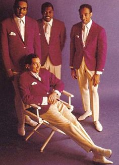 three men in red suits and white pants are posing for a photo while sitting on a chair