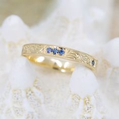 Discover the perfect blend of vintage beauty and modern glamor in this hand-engraved Sapphire Trio Vintage Wave Band. Set with 5 beautiful sapphires and crafted by hand in 18K Treasure Gold, made with reclaimed treasure from a sunken 17th-century ship, this stunning ring evokes timeless sophistication and luxurious style. The band features a total of 5- 1.5mm blue sapphires. The first 3 are grouped as a trio on the top of the band with the remaining two spaced between the engraved panels on eith Treasure Gold, Vintage Waves, Special Ring, Vintage Beauty, 17th Century, Hand Engraving, Blue Sapphire, 18k Gold, Sapphire