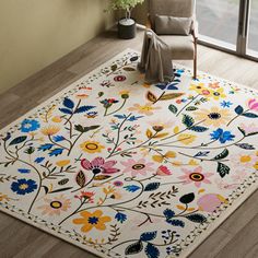 a white rug with colorful flowers on it in front of a chair and large window