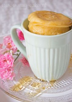 a white cup with some food in it on a glass plate next to pink flowers