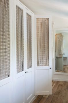 an empty room with white walls and wooden floors is pictured in this image, there are three doors that have decorative mesh panels on them