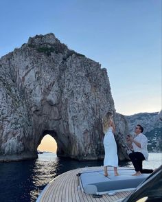 a man and woman standing on the bow of a boat in front of a rock formation