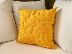 a yellow pillow sitting on top of a white couch next to two pillows with hearts drawn on them