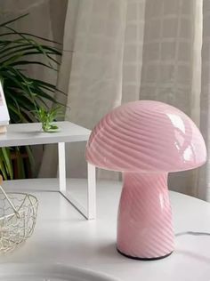 a pink lamp sitting on top of a white table next to a potted plant