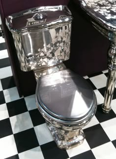 a silver toilet sitting on top of a black and white checkered floor next to a mirror