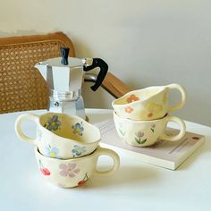 two flowered cups sitting on top of a table next to a coffee pot and grinder