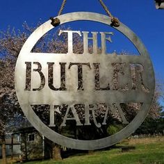 a metal sign that says the butler farm hanging from a chain in front of a tree