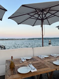 an outdoor dining area with tables and umbrellas overlooking the water at sunset or dawn