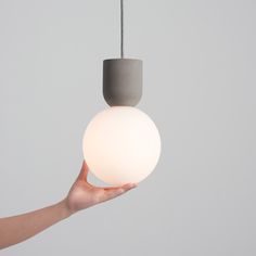 a hand holding a light that is on a gray wall with a white ball hanging from it